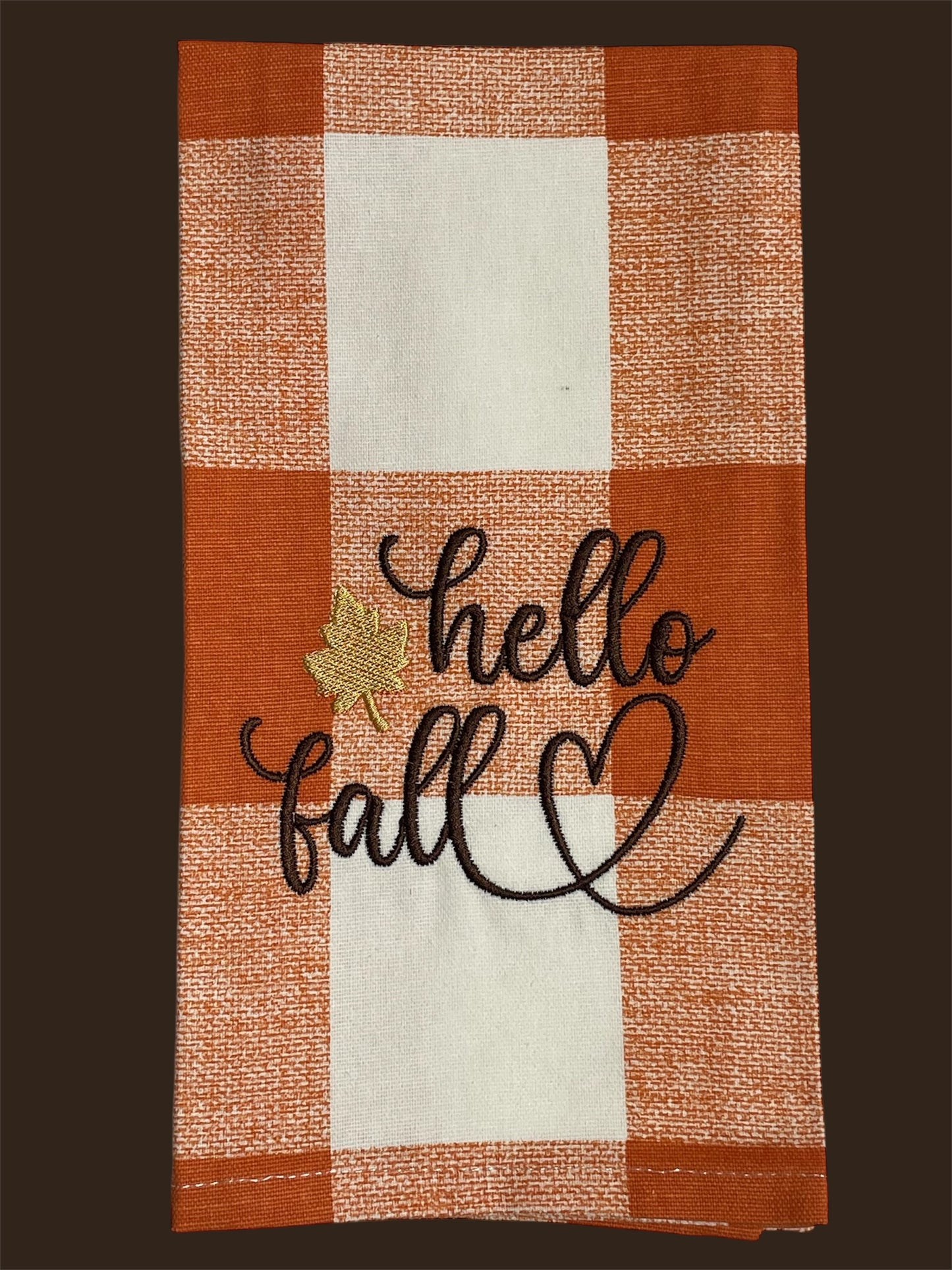 Seasonal hand towel with embroidered "hello fall" text, gold leaf accent, and heart design on an orange and white buffalo check background, ideal for autumn kitchen or home decor.