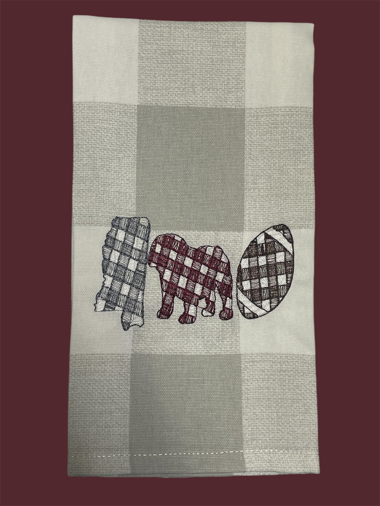 Decorative hand towel featuring embroidered Mississippi state outline, elephant, and football design in gingham patterns on neutral plaid background, perfect for Alabama fans and football-themed kitchen or game day decor.