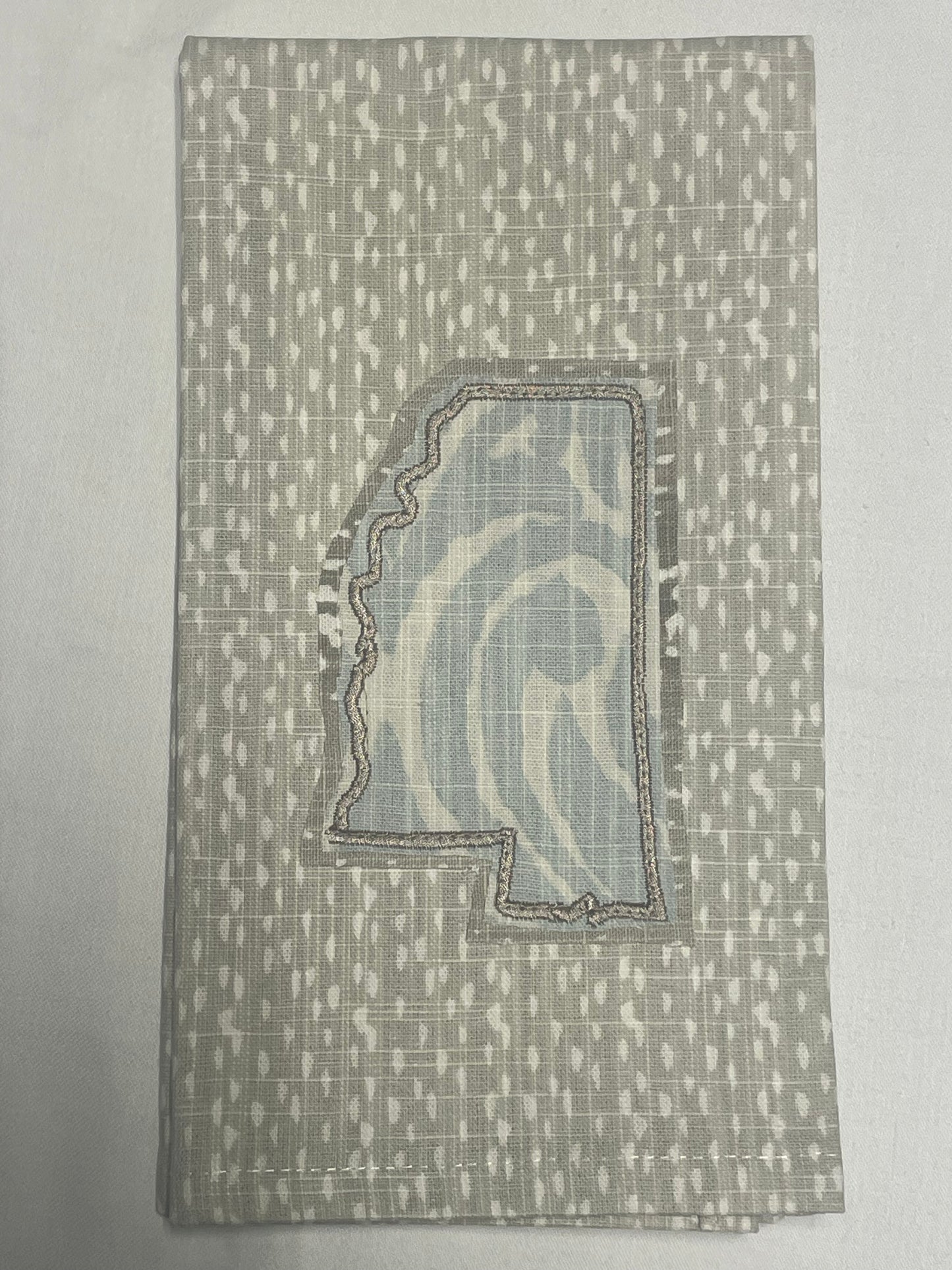 Decorative hand towel featuring embroidered Mississippi state outline with light blue abstract patterned fabric on neutral background, perfect for southern home decor and state pride gifts.