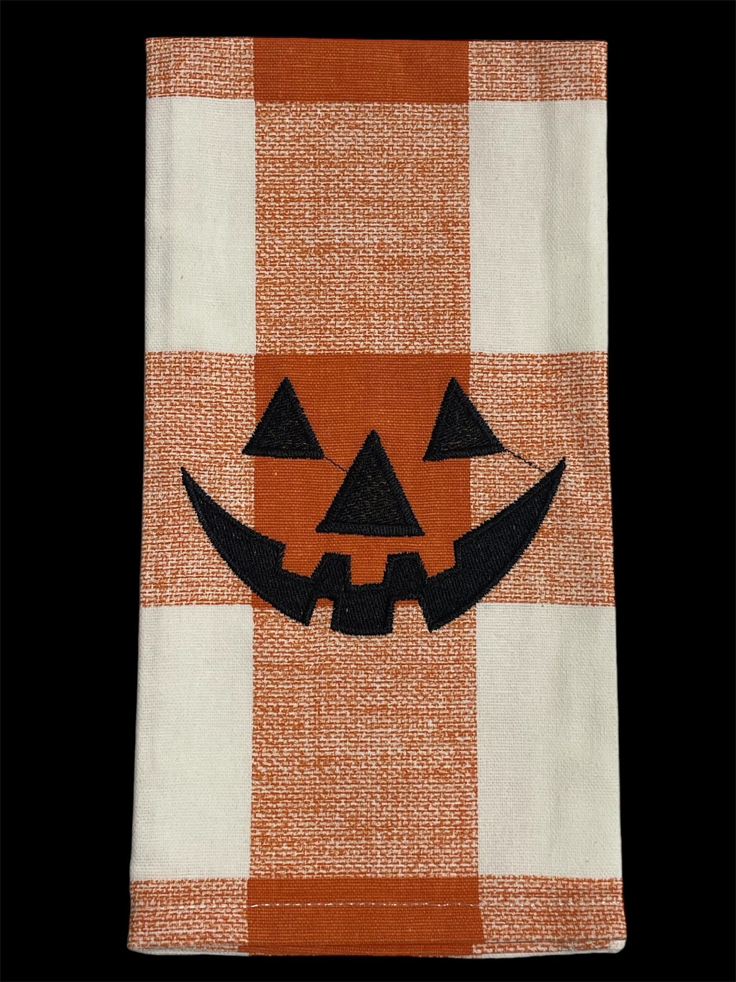 Festive hand towel featuring an embroidered black jack-o-lantern face on orange and white buffalo plaid background, perfect for Halloween kitchen or holiday decor.