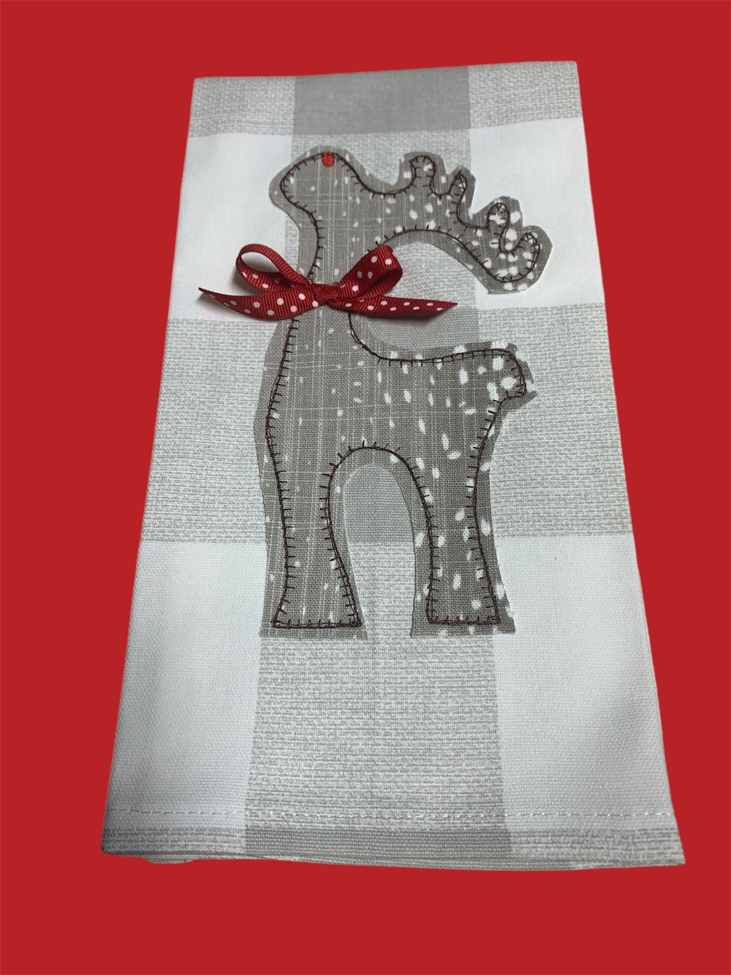 Decorative hand towel featuring embroidered reindeer silhouette with red polka dot bow and small red accent on antler, displayed on neutral plaid background, perfect for Christmas holiday decor.