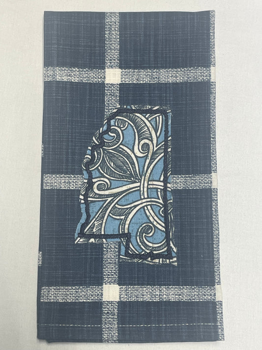 Decorative hand towel featuring embroidered Mississippi state outline with blue and white floral scroll pattern on dark blue plaid background, perfect for southern home decor and state pride gifts.