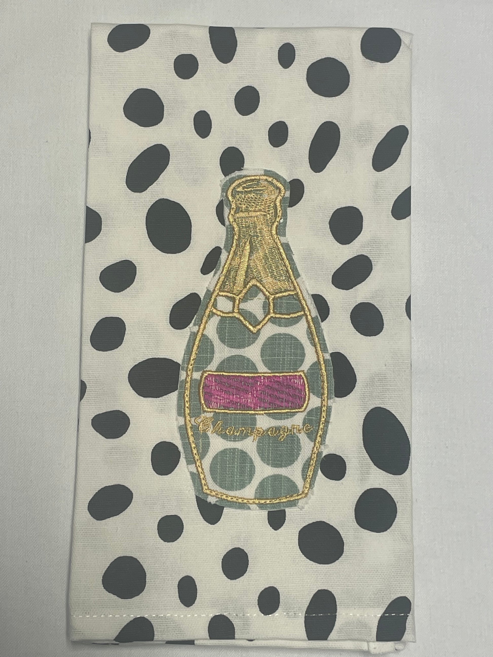 Decorative hand towel featuring embroidered champagne bottle with gold detailing and pink label on black polka dot background, perfect for celebrations, parties, and kitchen or bar decor.