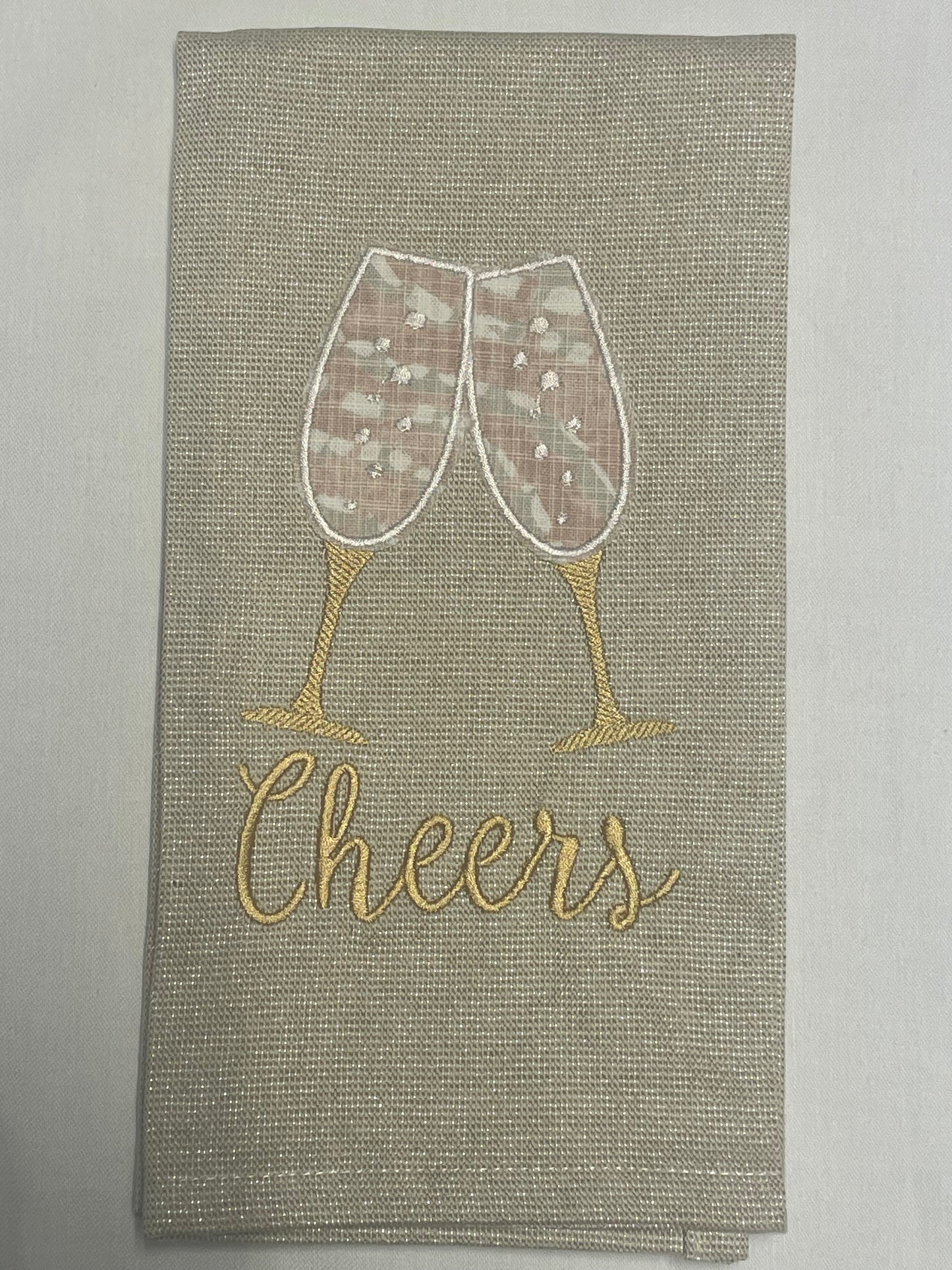 Decorative hand towel featuring embroidered champagne glasses clinking above “Cheers” text on neutral fabric, perfect for weddings, anniversaries, parties, and holiday celebrations.