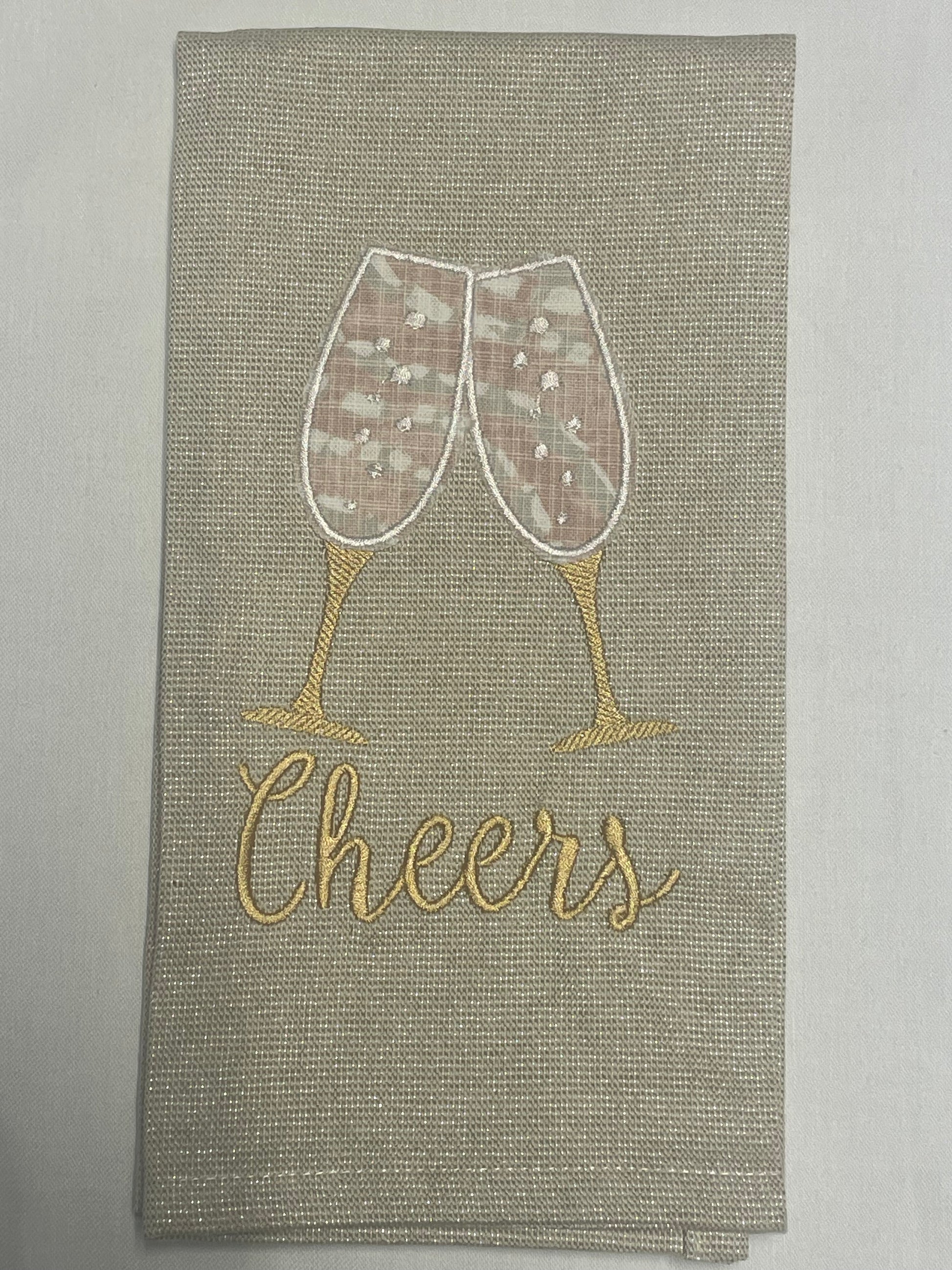 Decorative hand towel featuring embroidered champagne glasses clinking above “Cheers” text on neutral fabric, perfect for weddings, anniversaries, parties, and holiday celebrations.