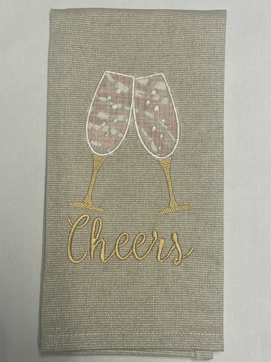 Decorative hand towel featuring embroidered champagne glasses clinking above “Cheers” text on neutral fabric, perfect for weddings, anniversaries, parties, and holiday celebrations.
