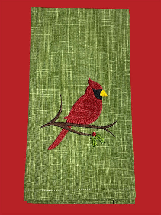 Decorative hand towel featuring embroidered red cardinal sitting on a branch with holly berries, displayed on a green textured background, perfect for Christmas or winter decor.