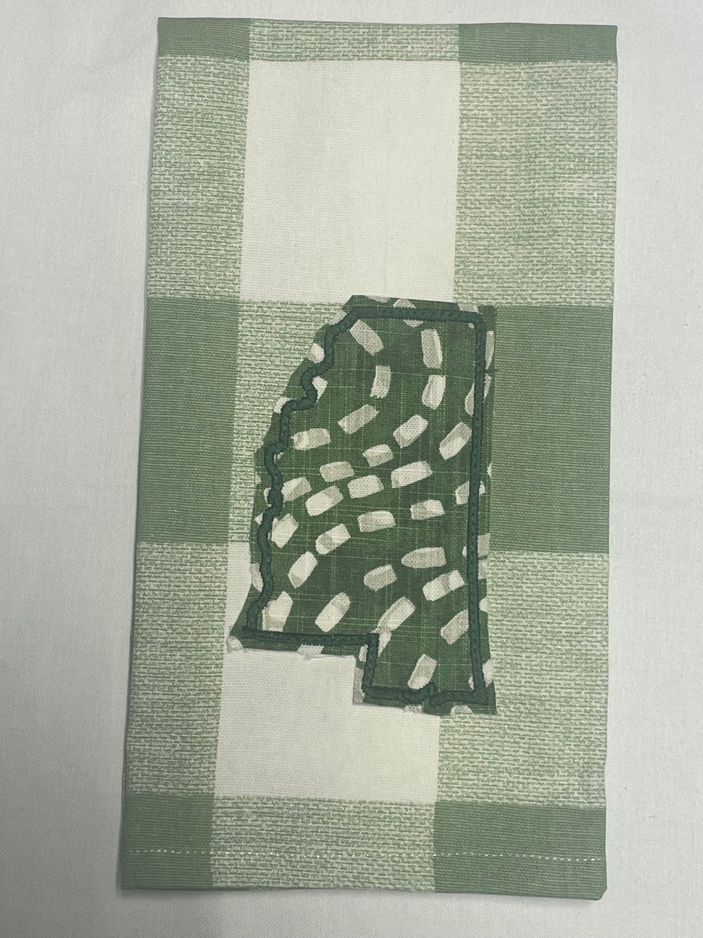 Decorative hand towel featuring embroidered Mississippi state outline with green and white abstract pattern on green plaid background, perfect for southern home decor and state pride gifts.