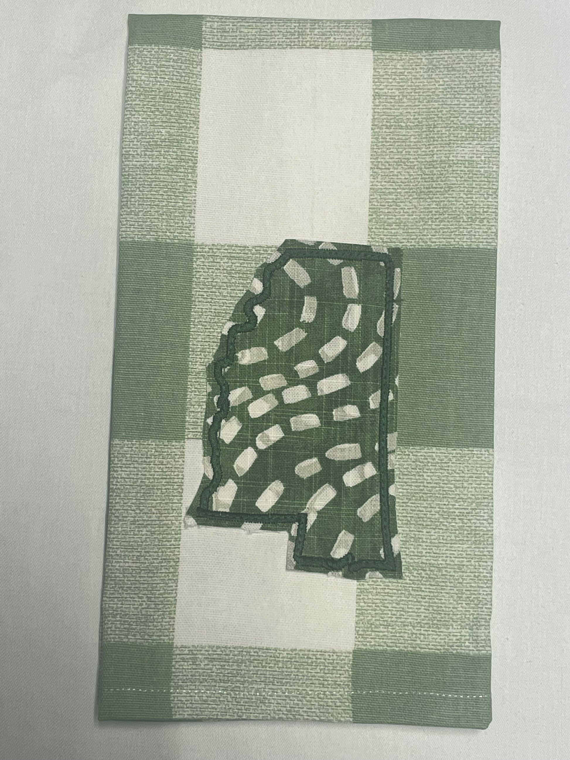 Decorative hand towel featuring embroidered Mississippi state outline with green and white abstract pattern on green plaid background, perfect for southern home decor and state pride gifts.