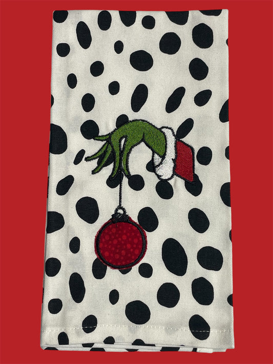Decorative hand towel with black polka dot background featuring embroidered green Grinch hand holding red Christmas ornament, perfect for holiday decor, gifting, or kitchen accents.