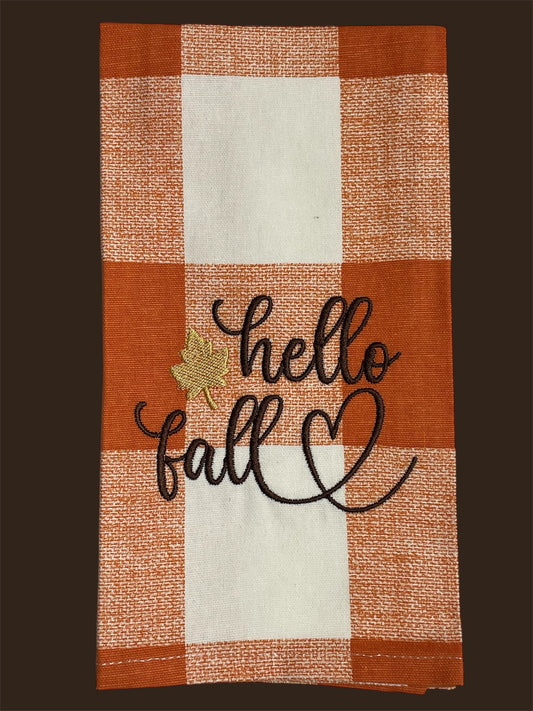 Seasonal hand towel with embroidered "hello fall" text, gold leaf accent, and heart design on an orange and white buffalo check background, ideal for autumn kitchen or home decor.