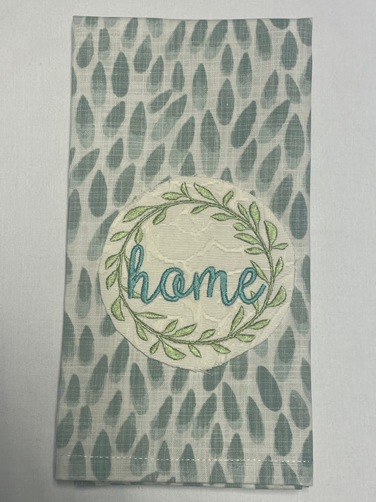 Decorative hand towel featuring embroidered "home" text inside a green leaf wreath on a blue and white abstract patterned background, perfect for everyday farmhouse kitchen or home decor.