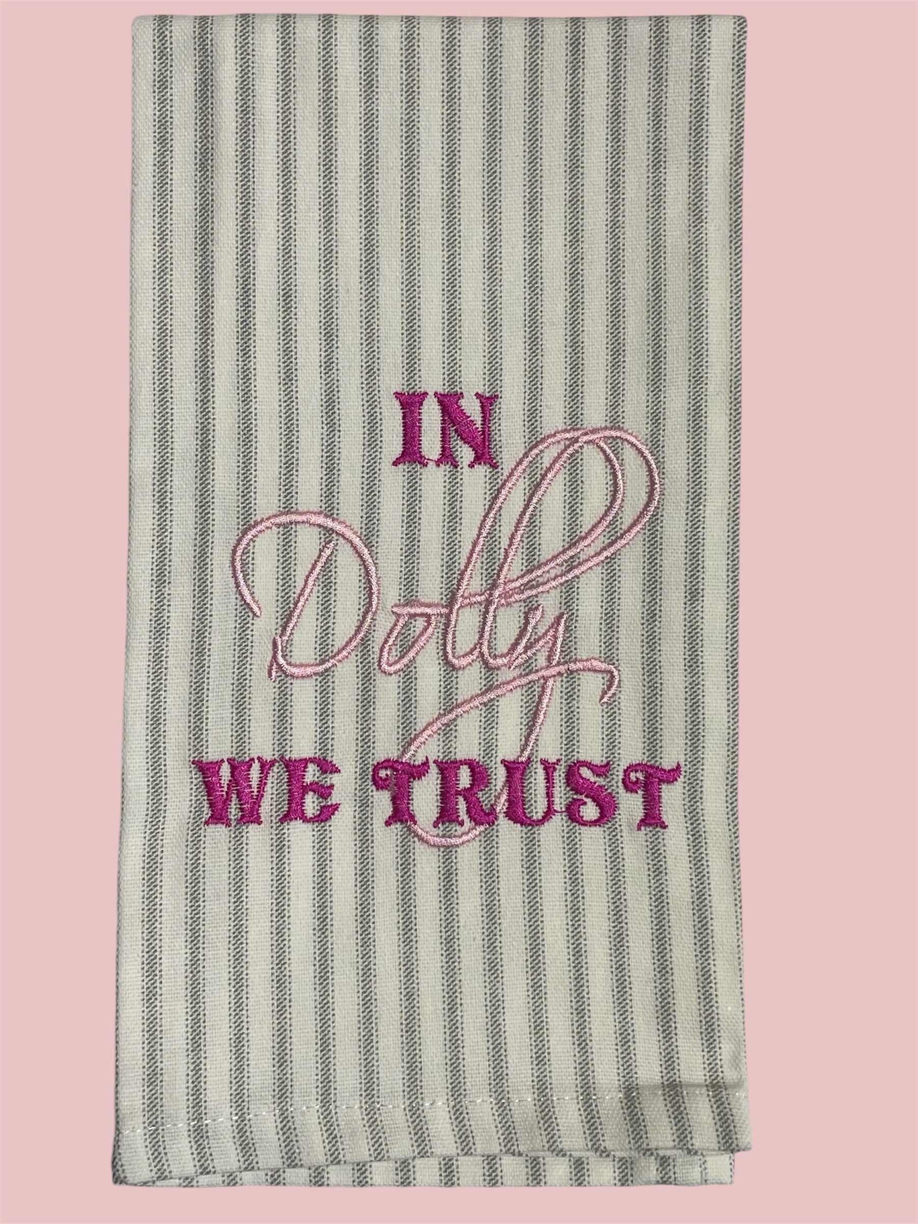 Striped decorative hand towel with embroidered text "In Dolly We Trust" in pink and magenta thread, perfect for Dolly Parton fans, Southern decor, and unique kitchen accents.