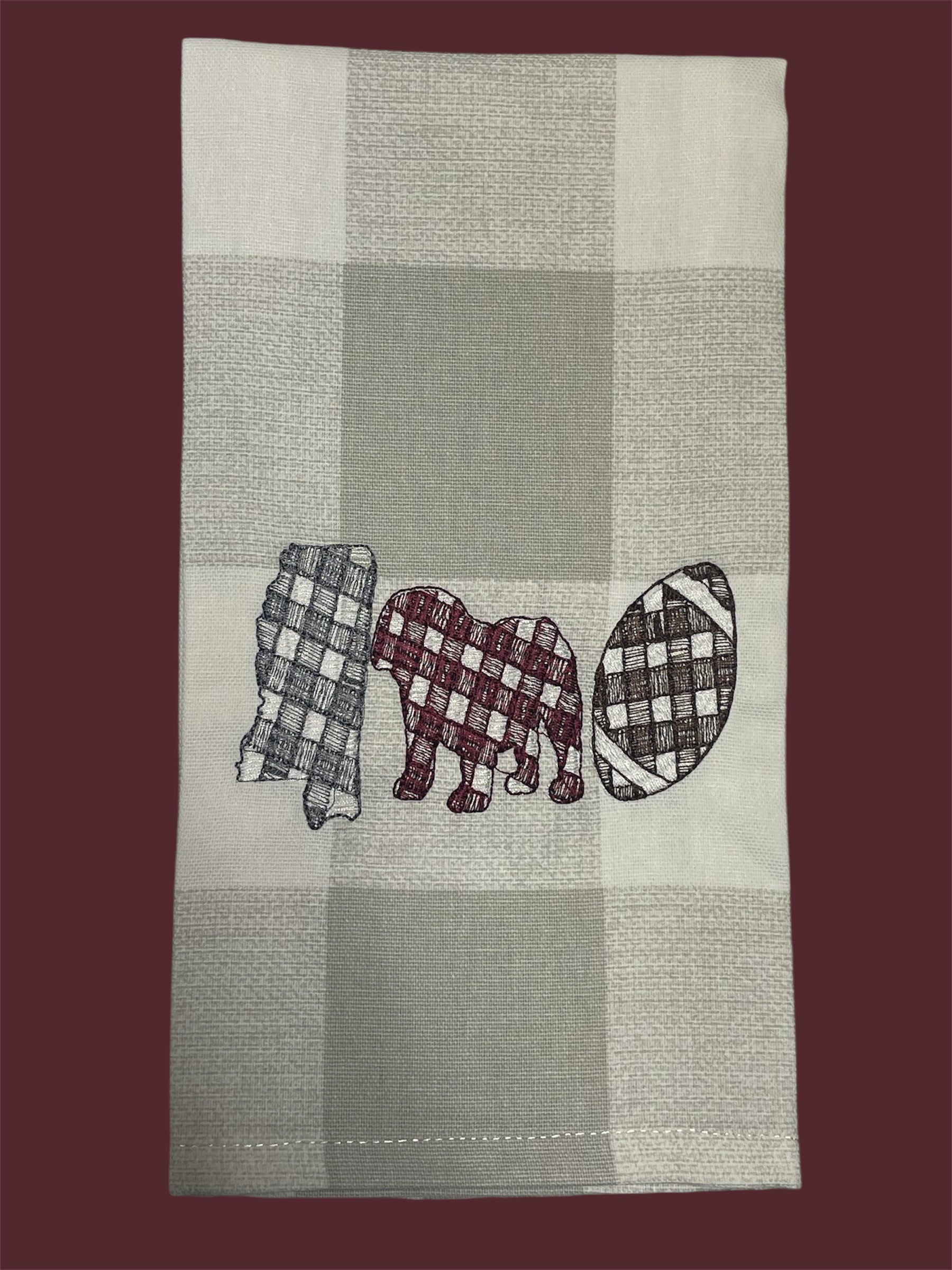 Decorative hand towel featuring embroidered Mississippi state outline, elephant, and football design in gingham patterns on neutral plaid background, perfect for Alabama fans and football-themed kitchen or game day decor.