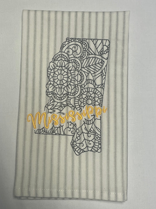 Decorative hand towel featuring embroidered Mississippi state outline with intricate lace design and yellow “Mississippi” script on gray striped background, perfect for southern home decor and state pride gifts.