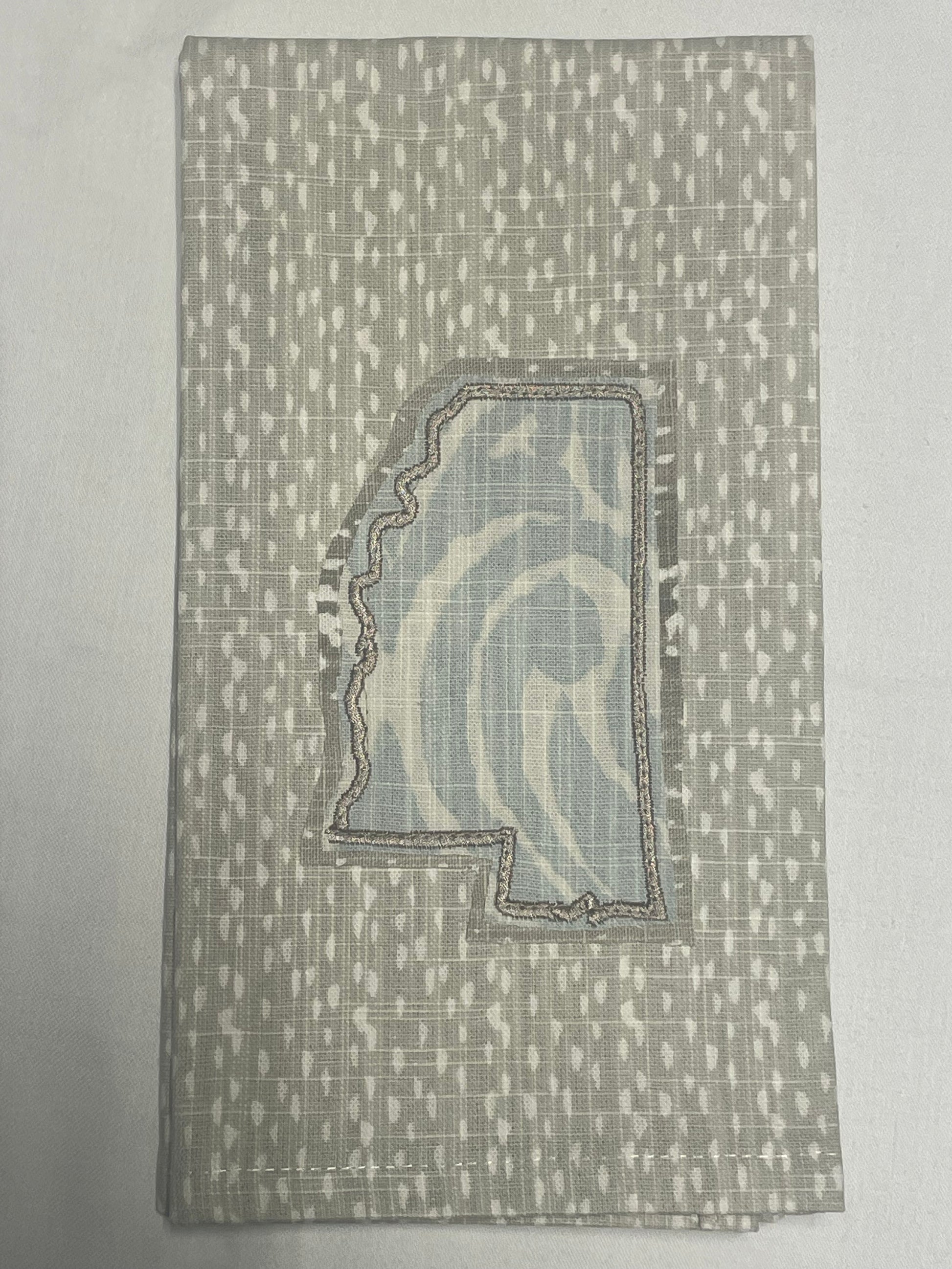 Decorative hand towel featuring embroidered Mississippi state outline with light blue abstract patterned fabric on neutral background, perfect for southern home decor and state pride gifts.