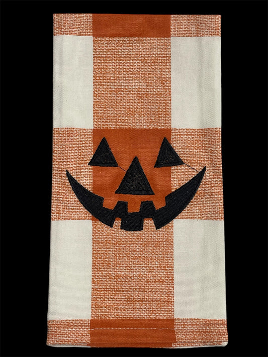 Festive hand towel featuring an embroidered black jack-o-lantern face on orange and white buffalo plaid background, perfect for Halloween kitchen or holiday decor.